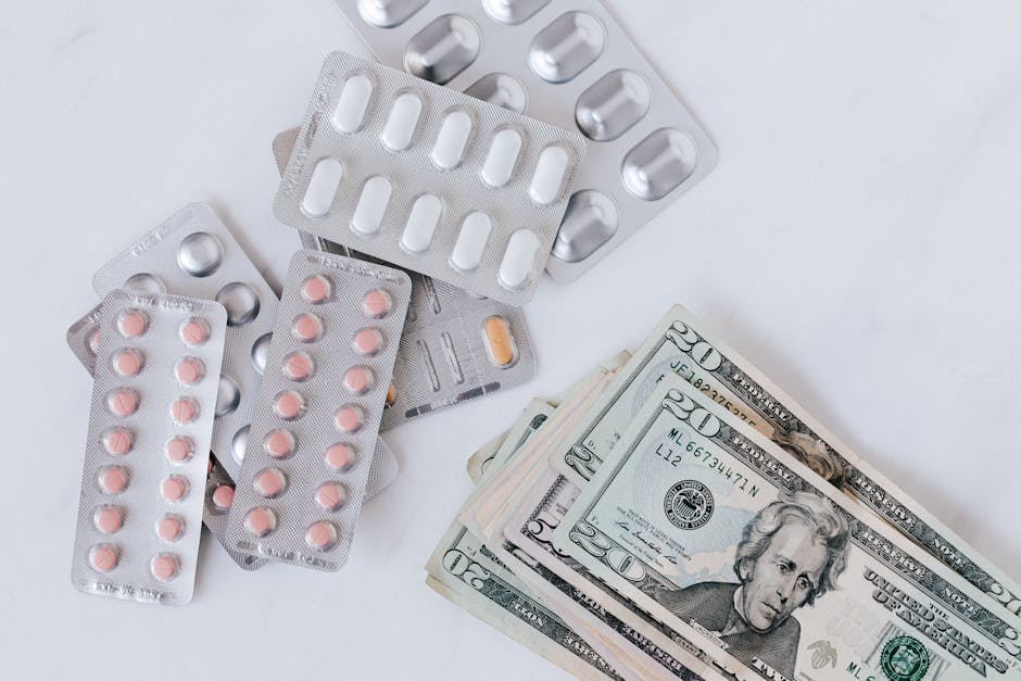 A collection of various blister packs of pills and capsules in different shapes and colors, including white, pink, and orange, arranged on a white surface alongside several folded US twenty-dollar bil